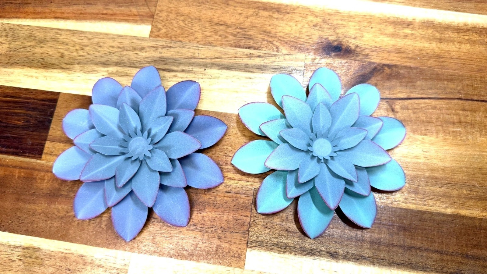 Small, teal-colored metal wall art feature is a layered flower design with disti