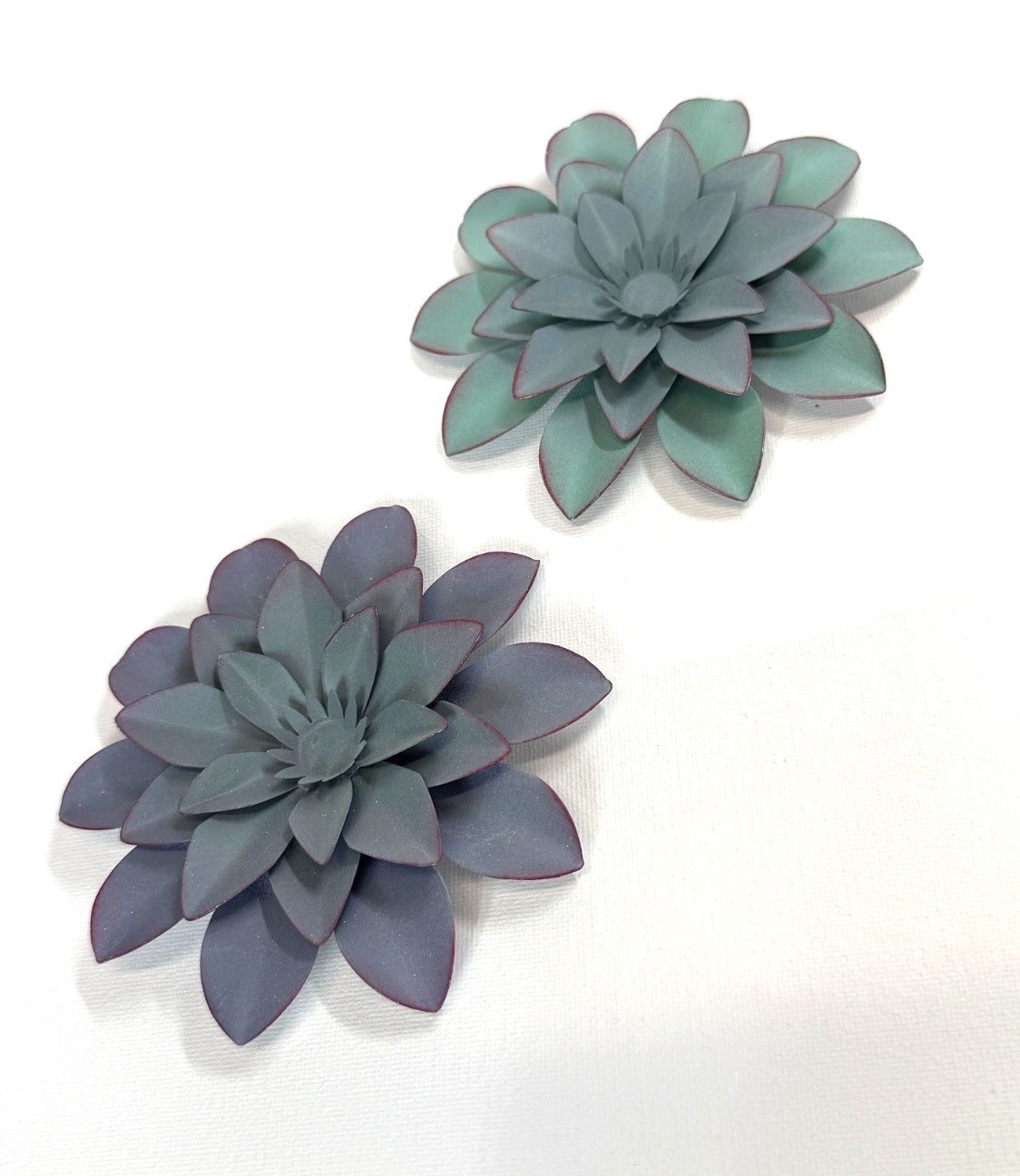 Small, teal-colored metal wall art feature is a layered flower design with disti