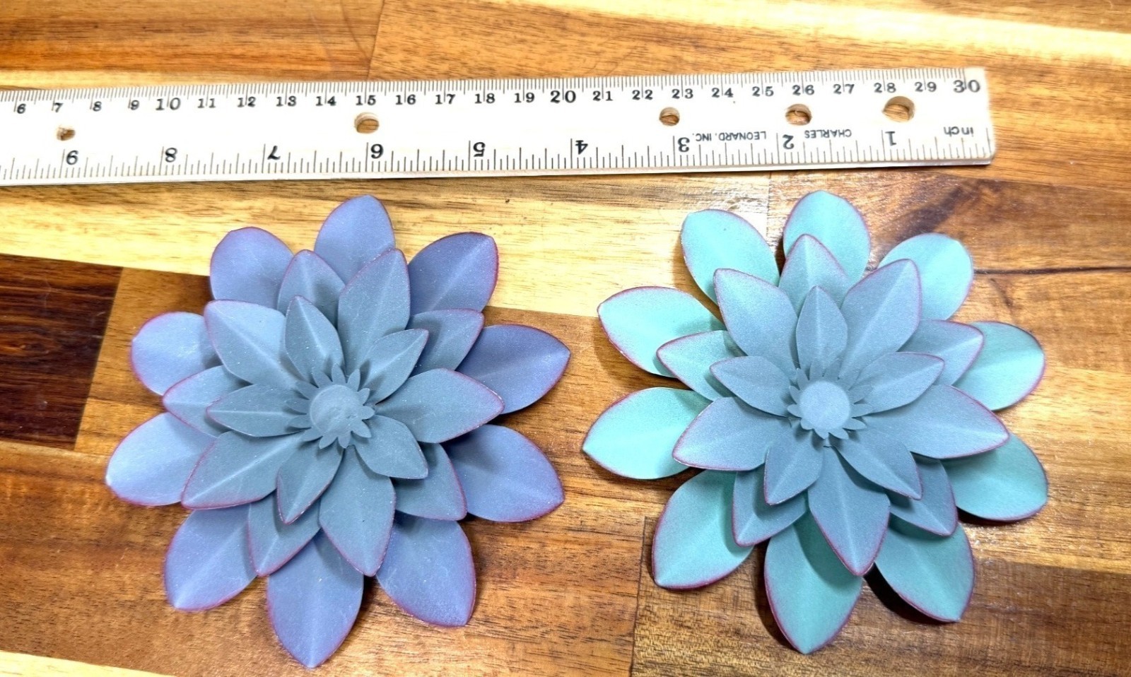 Small, teal-colored metal wall art feature is a layered flower design with disti