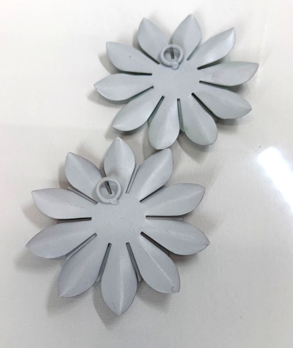 Small, teal-colored metal wall art feature is a layered flower design with disti